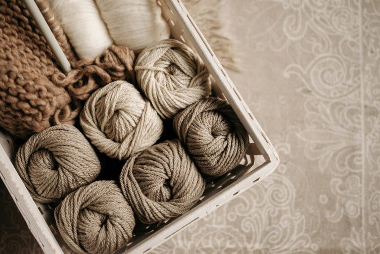 Basket filled with warm-toned yarn balls on patterned fabric, ideal for crafting inspiration.