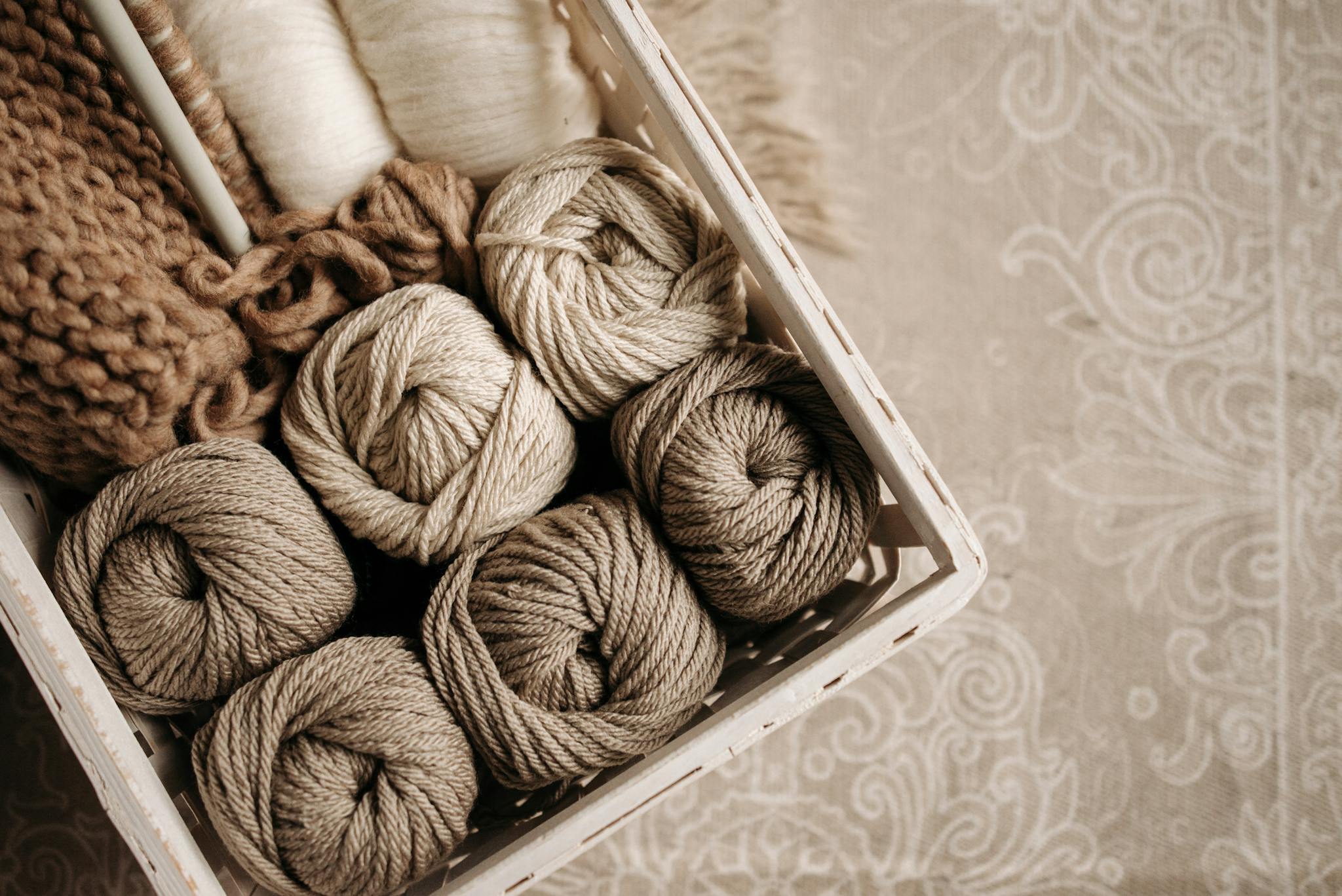 Basket filled with warm-toned yarn balls on patterned fabric, ideal for crafting inspiration.