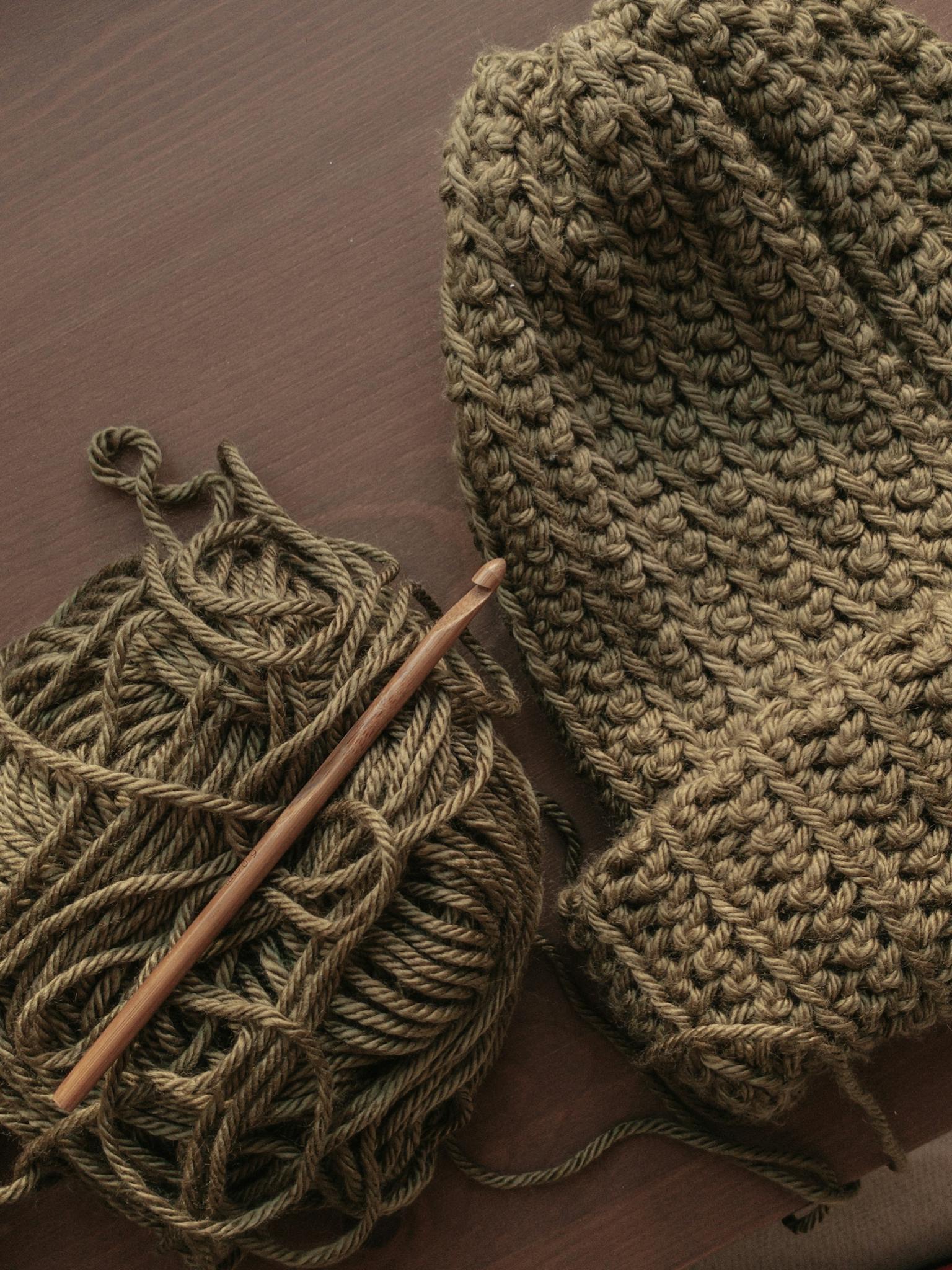 Handcrafted knit hat with yarn and crochet hook on a wooden table.