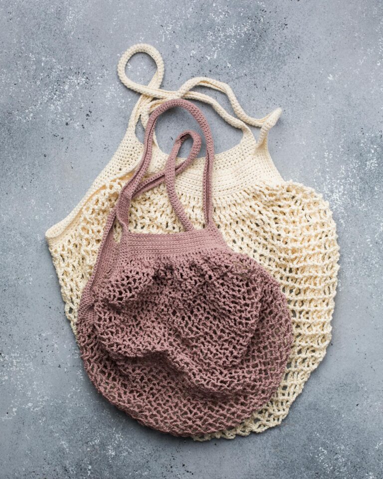 Two knitted reusable mesh bags in beige and pink, ideal for eco-friendly shopping.